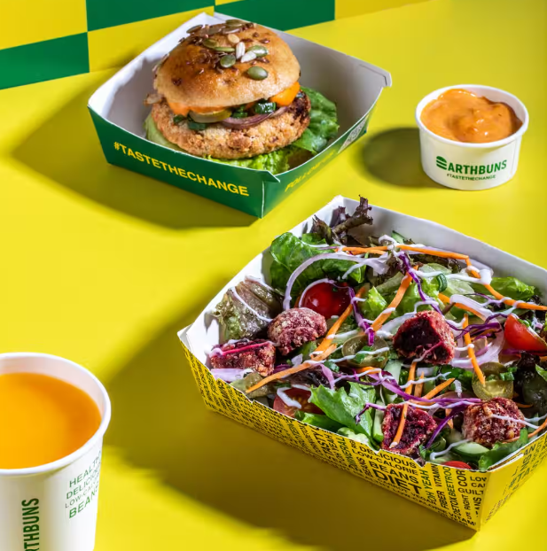 Earth Buns burger, salad and sauces on a yellow table
